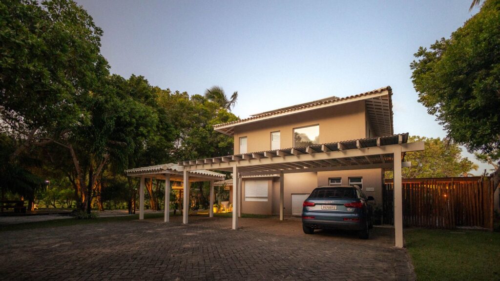 Custom-built modern home with pergola and driveway at twilight, surrounded by landscaping