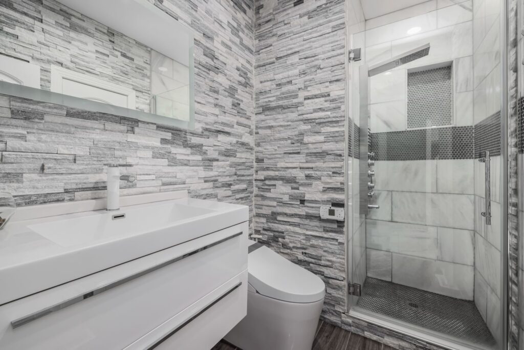 Modern luxury bathroom remodel with glass shower, stone walls, and sleek white vanity in Westchester NY