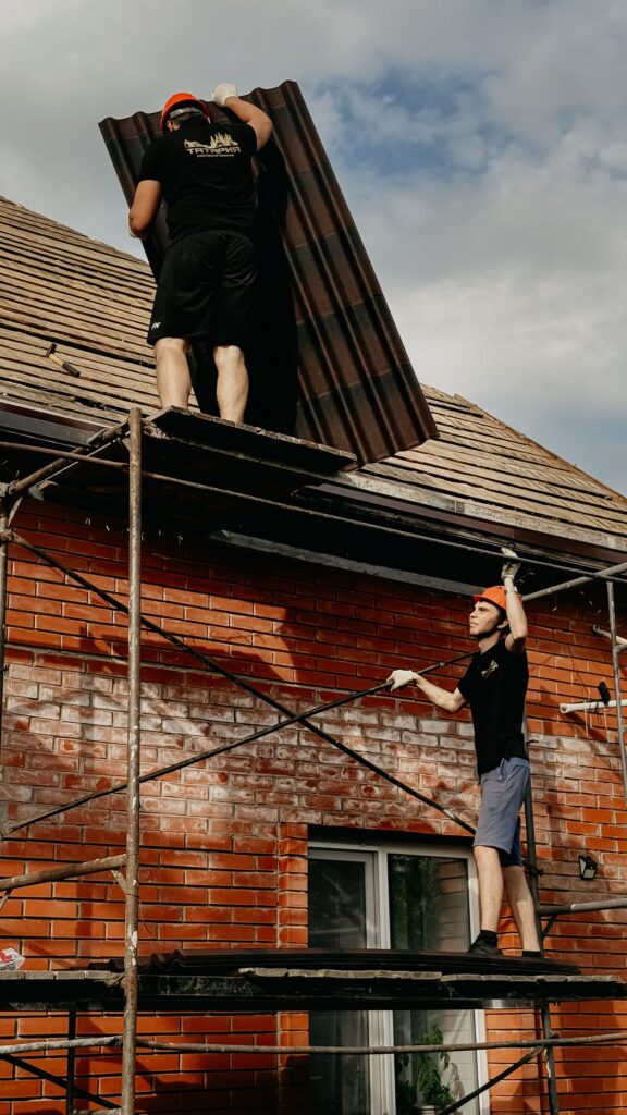 Roofing crew on scaffolding installing panels on a brick building roof