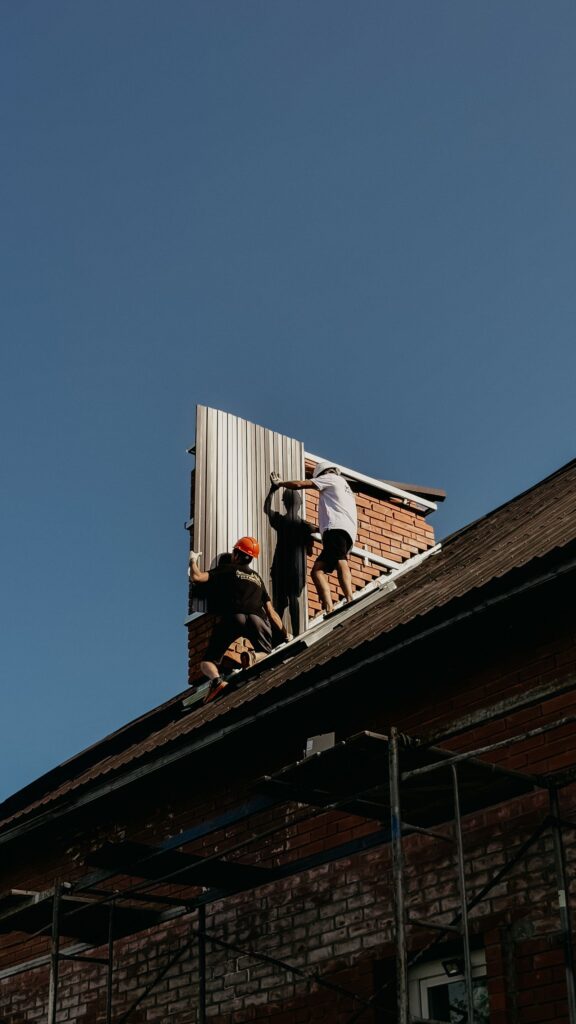 Roofing crew installing metal roof panels on a brick home under clear skies